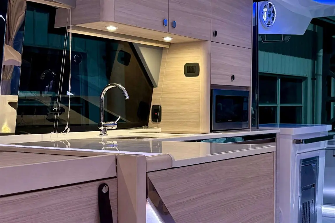 Modern kitchen with wooden cabinetry, a sleek sink, integrated microwave, and illuminated work surfaces in a stylish setting.